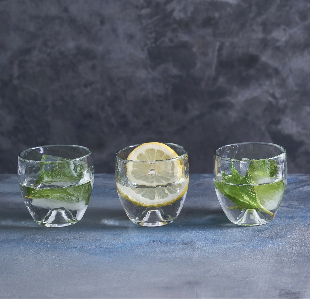 Three matching pebbled drinking glasses styled with water, lemon and mint