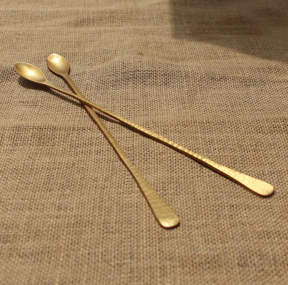 Two long hammered brass bar spoons on natural woven fabric