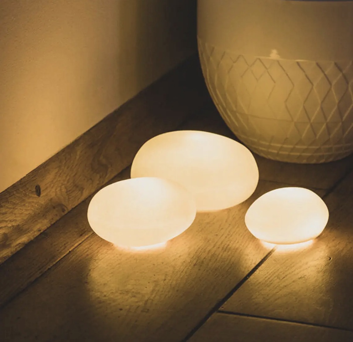 Set of three lit matte-porcelain Light Pebbles glowing on a dark wood floor