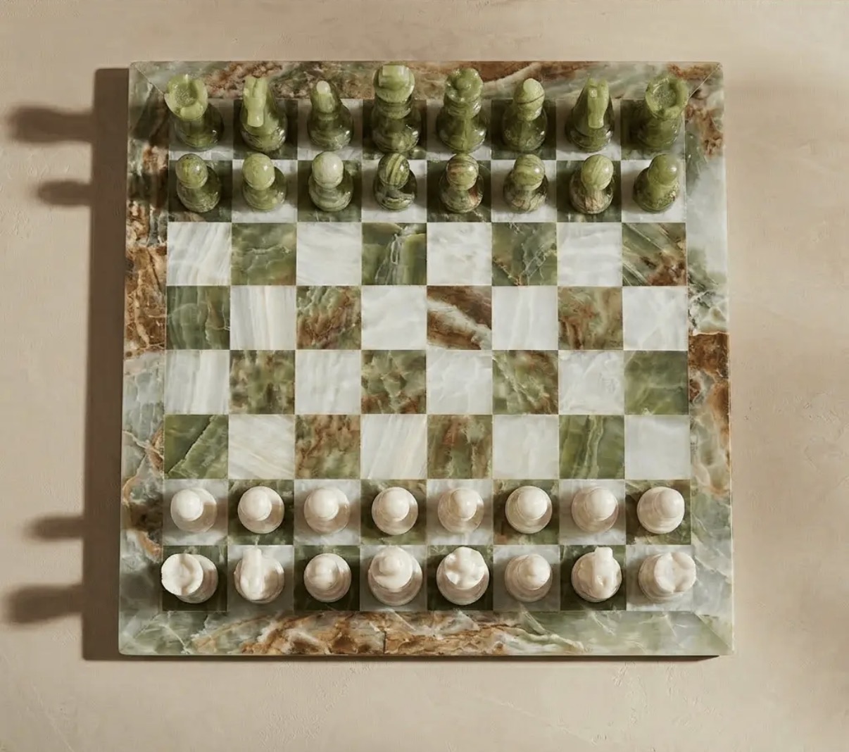 Overhead view of the green onyx and white marble chess set with carved pieces lined up across the checkered stone board