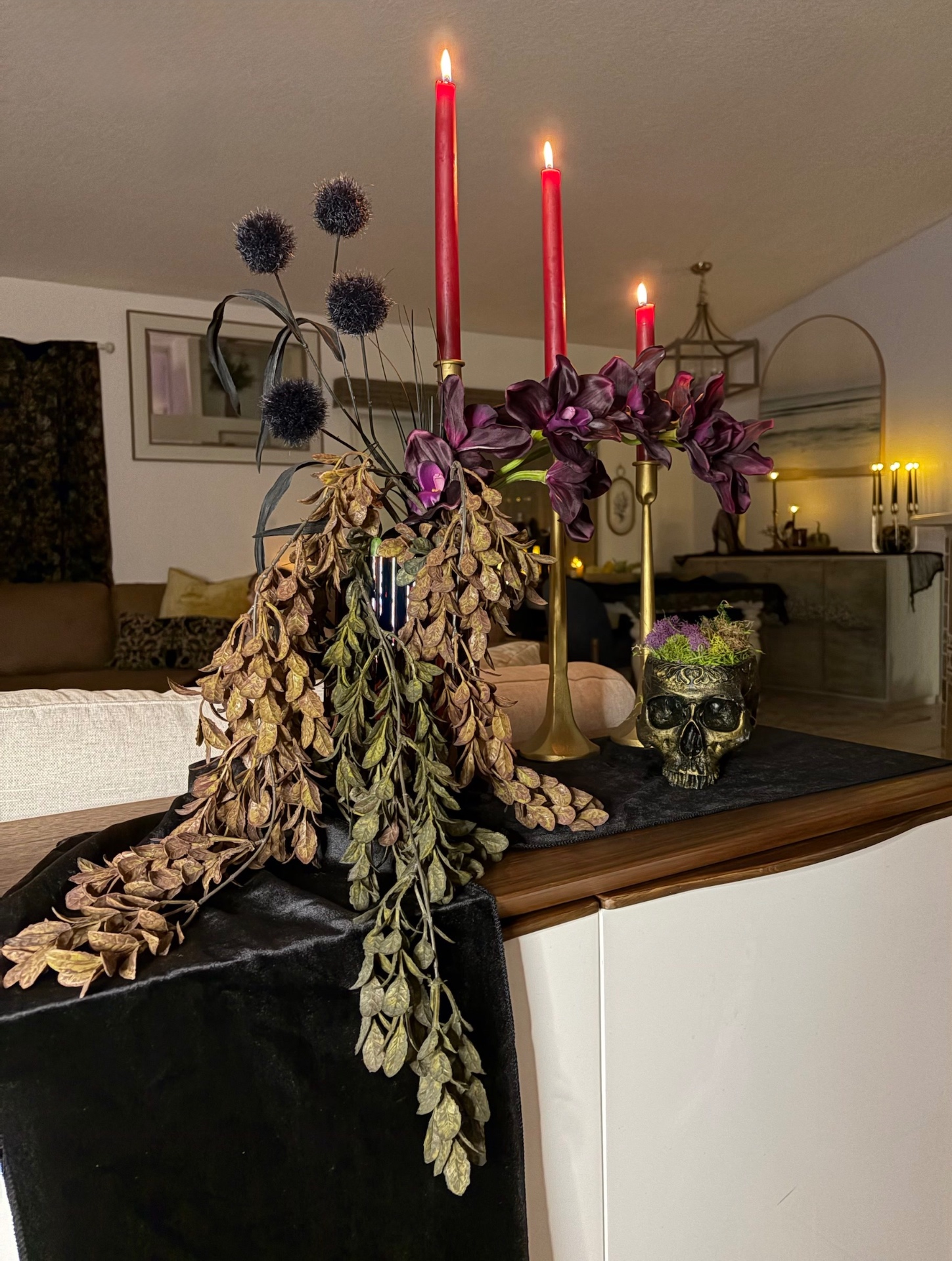 The wooden console styled with the After Dark box — black velvet runner, brass candlesticks, lit red tapers, plum florals and a moss-filled skull planter