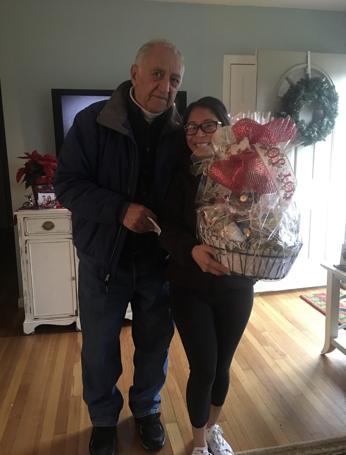 A family photograph: Ashley stands beside her grandfather holding a gift hamper topped with a red bow