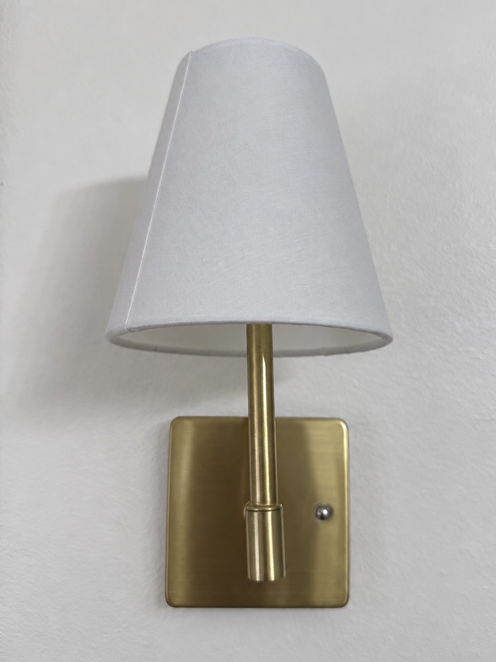 Rechargeable brass wall sconce with a white fabric shade
