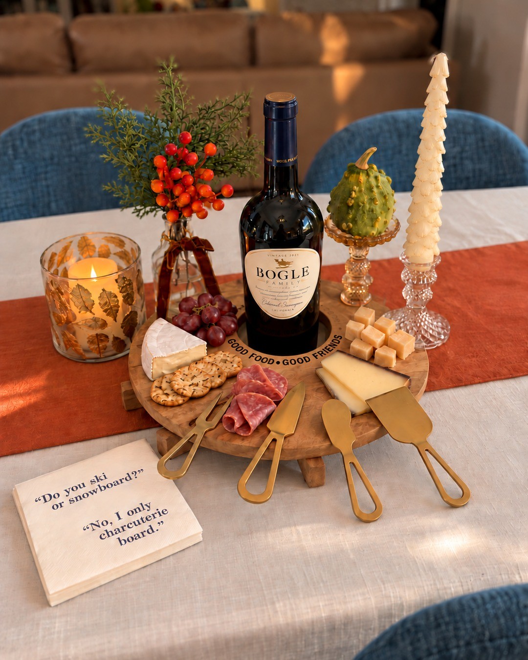 The Board Meeting styled on a warm holiday table with a mango wood wine board, four gold cheese knives and charcuterie napkins