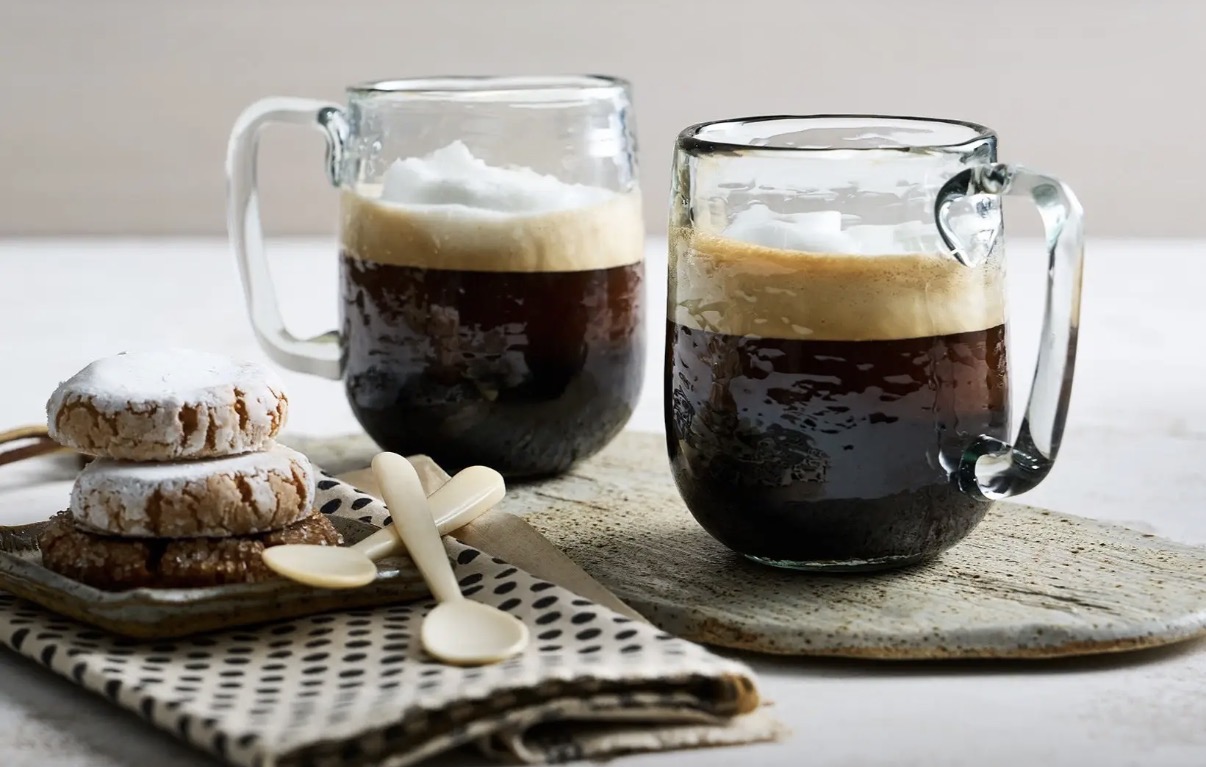 Two pebbled glass mugs filled with coffee beside cookies