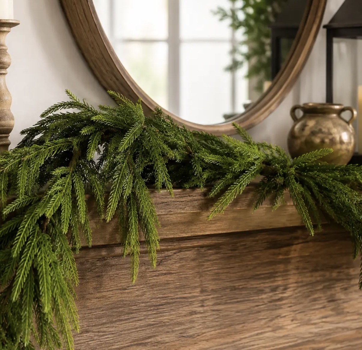 Norfolk pine garland draped over a wooden mantel beneath a round mirror