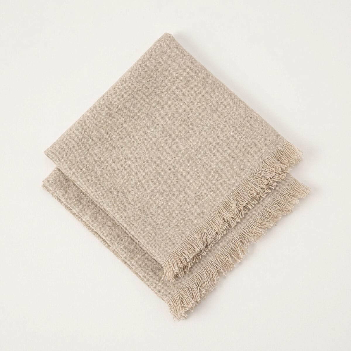Two natural-fringe dinner napkins stacked on a neutral surface